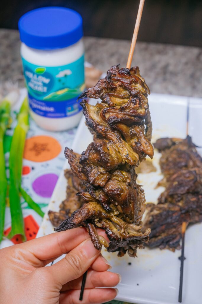 Grilled jerk oyster mushroom skewer with caramelized glaze and plant-based ingredients in background.